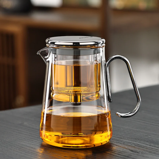 Clear glass teapot with silver handle and lid on a wooden tabletop