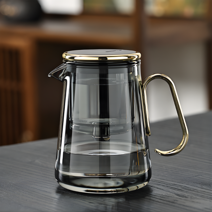 Clear glass teapot with gold handle and lid on a wooden tabletop